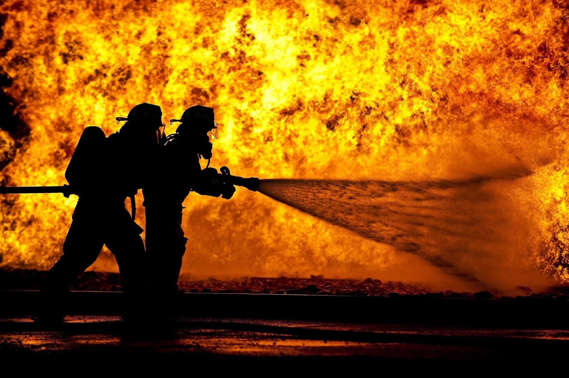 two fire fighters tackling a raging fire in the background